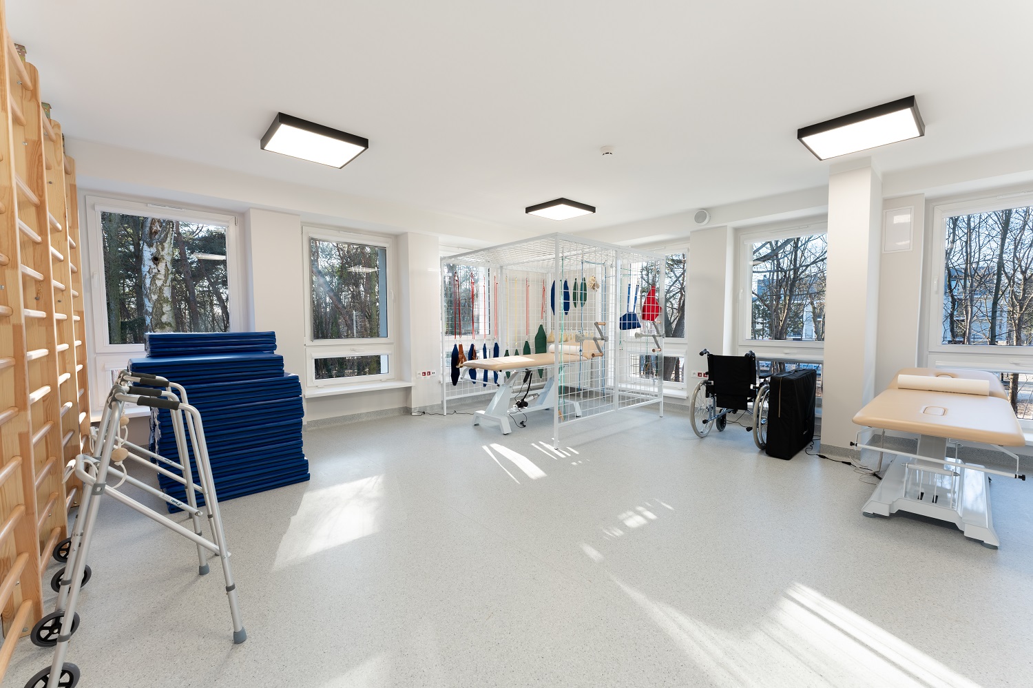 Sala rehabilitacji z drabinkami, materacami, chodzikiem, stołami terapeutycznymi i klatką UGUL